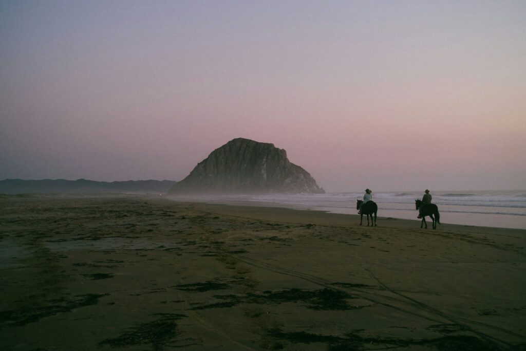 Two people riding horses at the beach at sunset in Morro Bay, California.